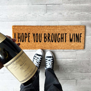 brown door mat that says "I hope you brought wine"