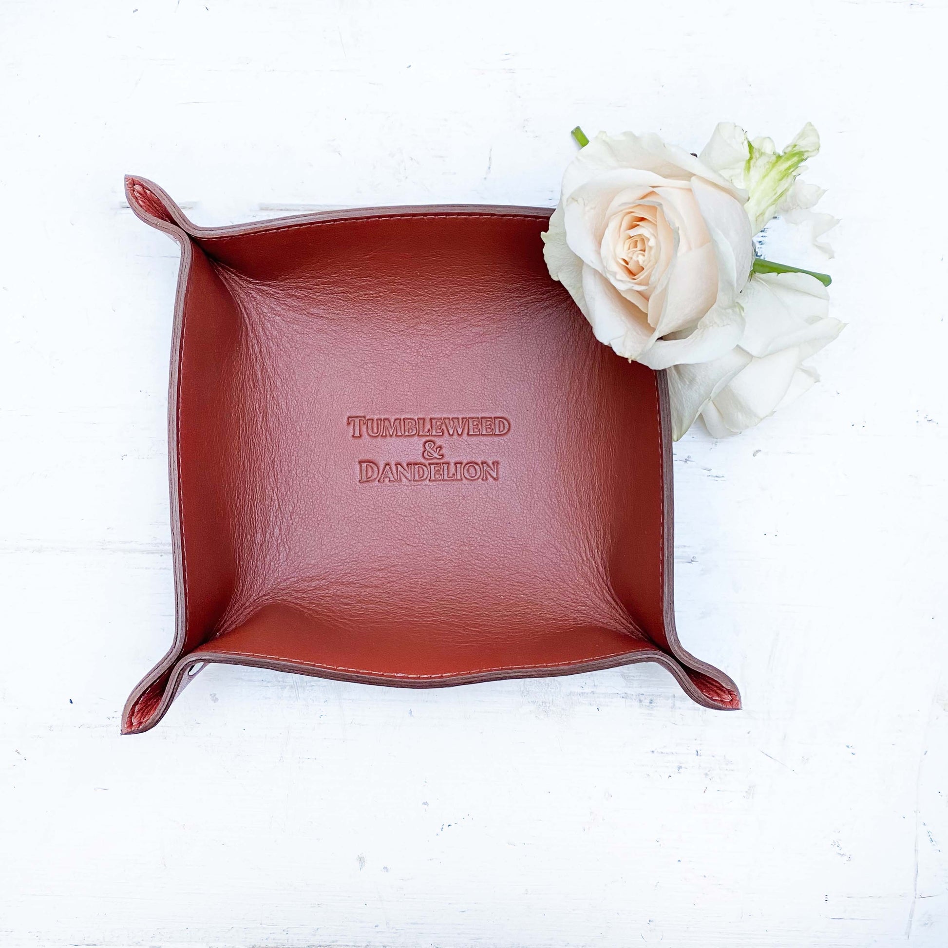 brown leather catch all tray with "tumbleweed and dandelion" embossed in the middle