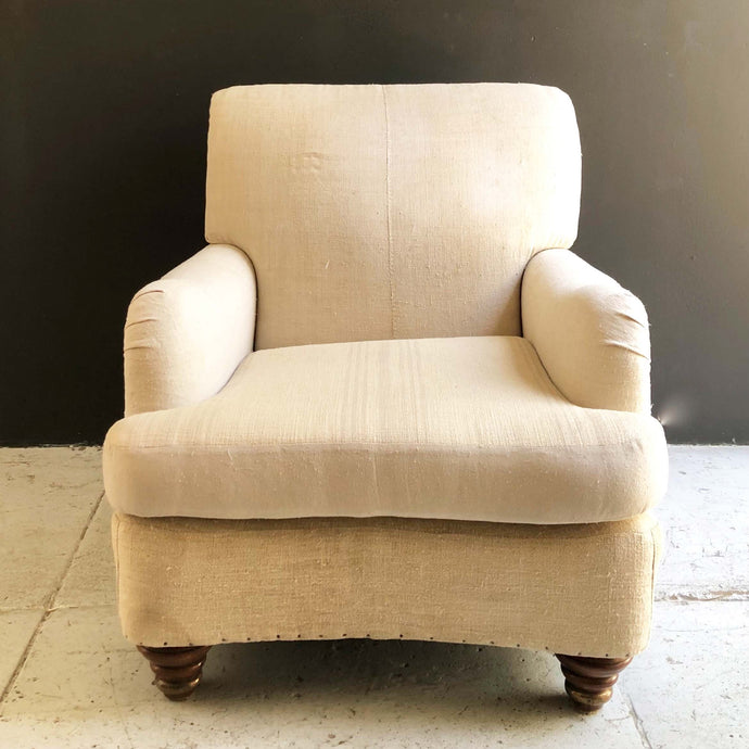 cream colored vintage feed sack cloth upholstered lounge chair with brown wooden feet and upholstery tacks