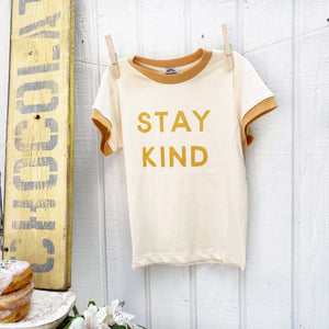 cream colored kid's tee shirt with amber accent around neck and sleeves with words "stay kind" on front