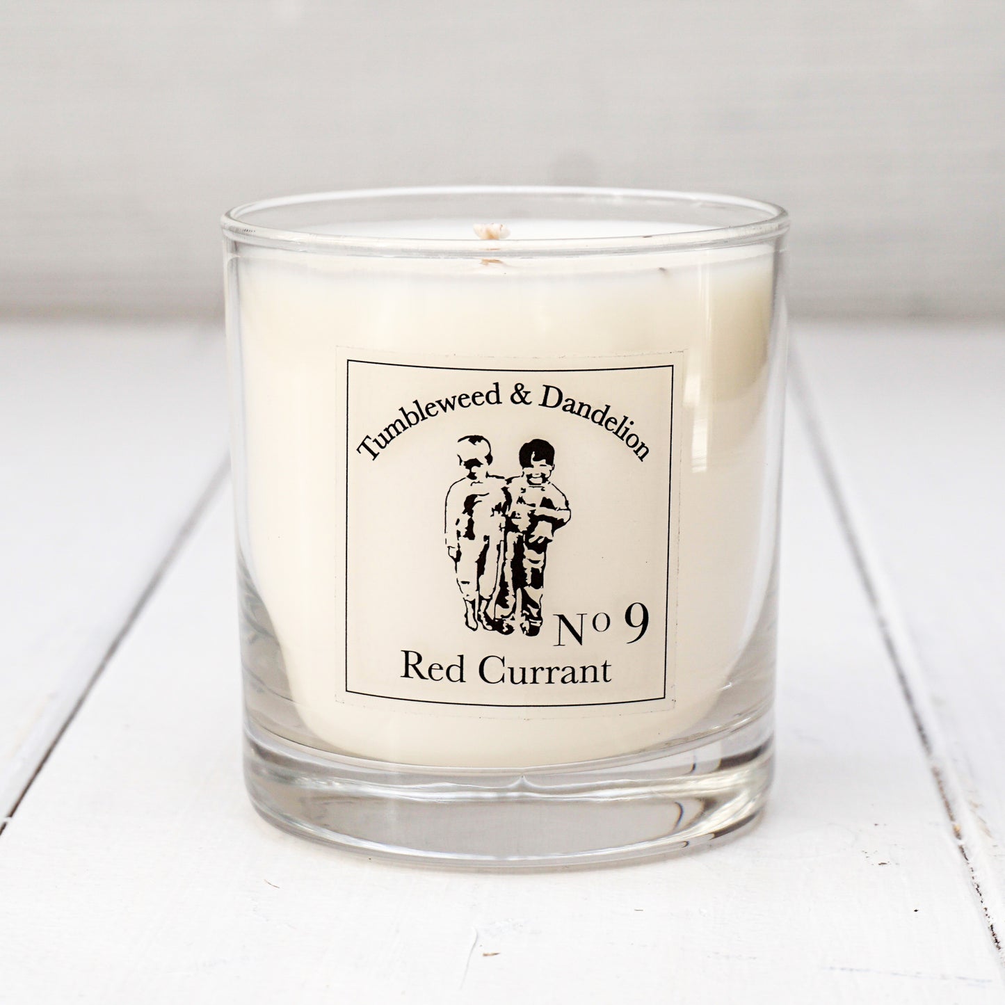 Clear glass candle, Tumbleweed and Dandelion logo, red currant scent