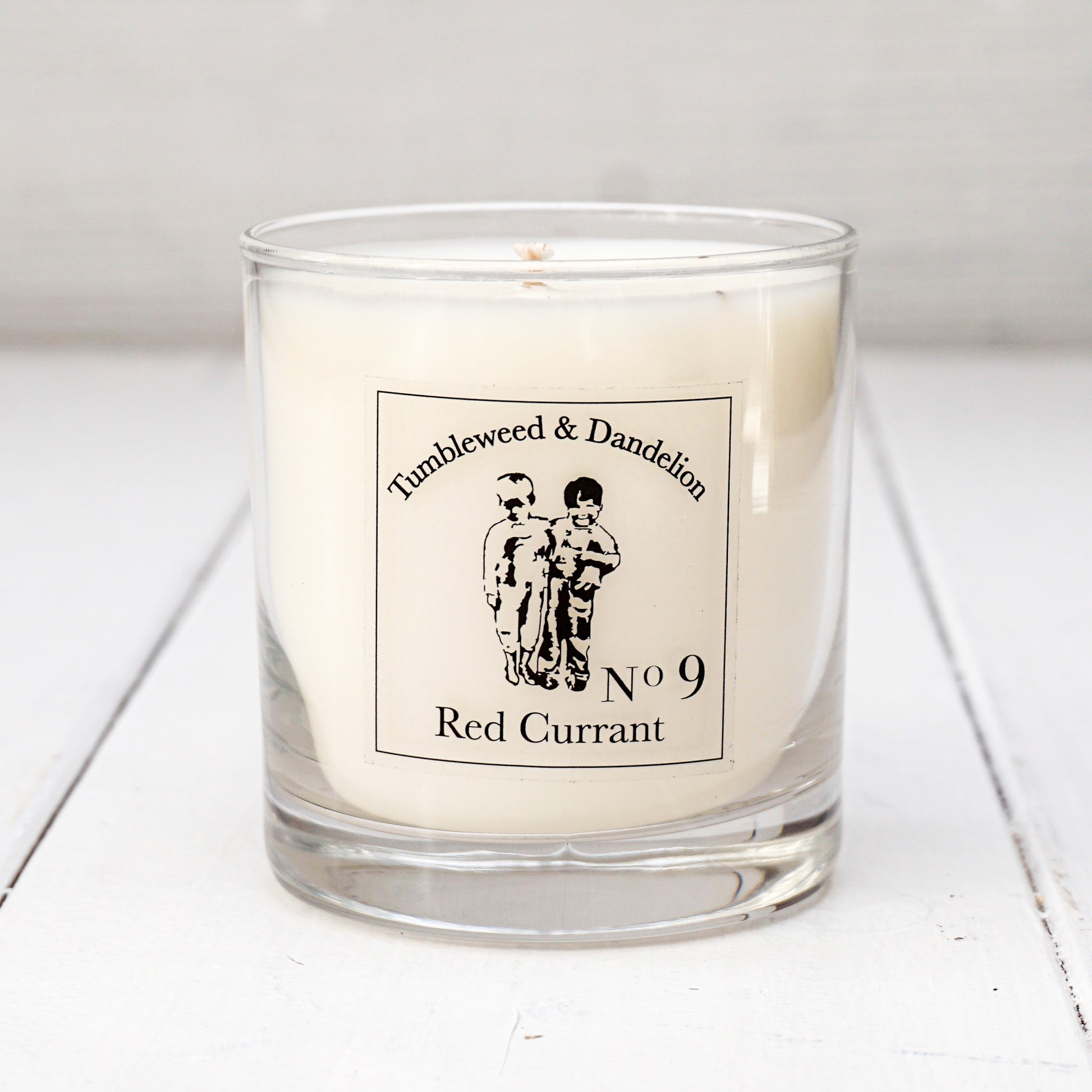 Clear glass candle, Tumbleweed and Dandelion logo, red currant scent