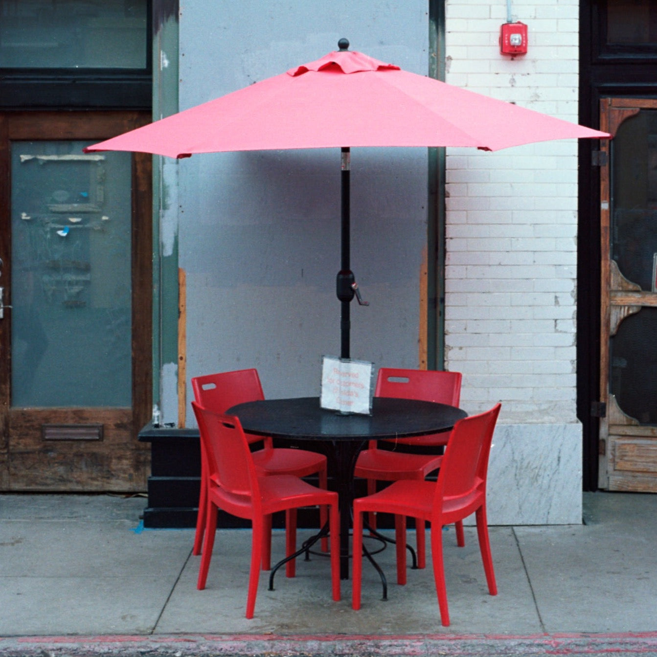 photo of a red umbrella, black table and four red chairs outside of a cafe