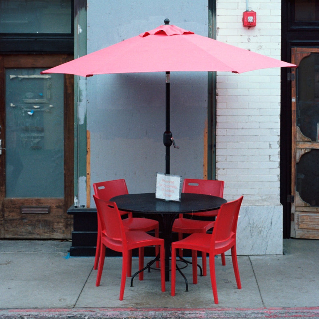 photo of a red umbrella, black table and four red chairs outside of a cafe