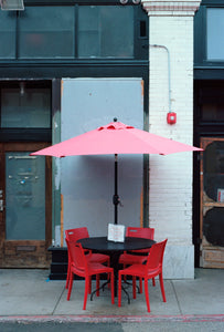 photo of a red umbrella, black table and four red chairs outside of a cafe