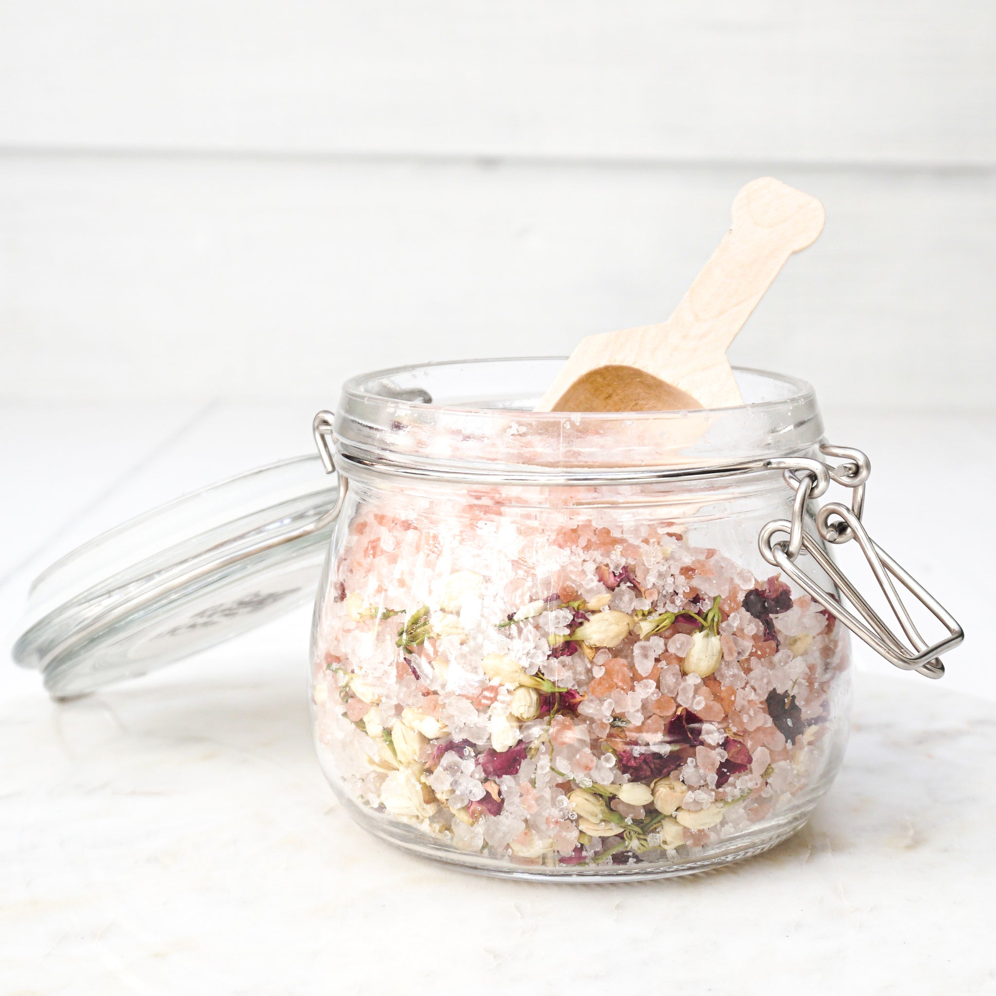 pink bath salts with herbs in clear glass jar with clamp lid and wood scoop